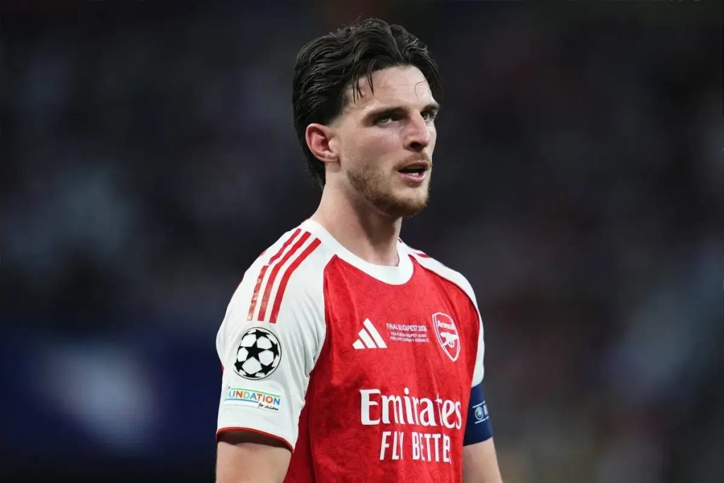 Jogador de camisola vermelha e branca do Arsenal, com a braçadeira de capitão, olhando para o lado durante um jogo da Liga dos Campeões.
