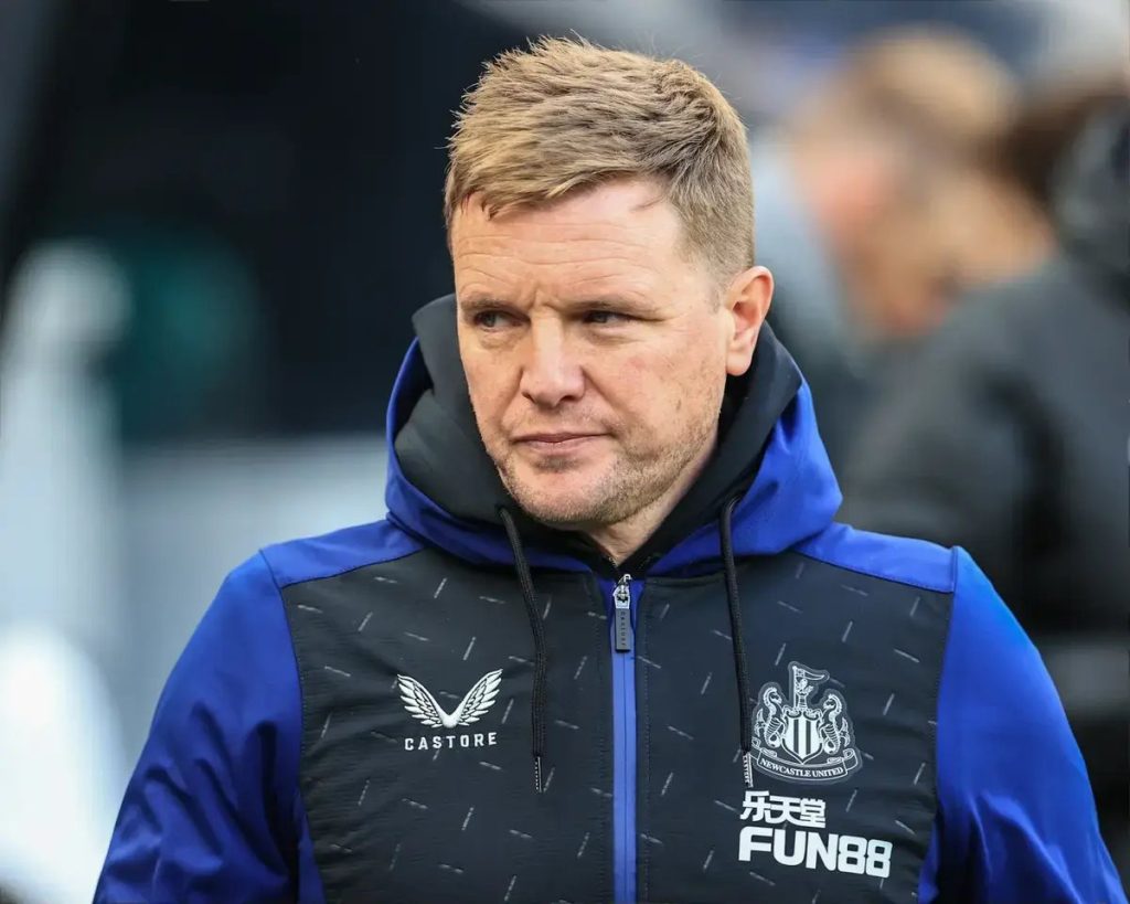 Treinador de casaco azul e preto com o logótipo do Newcastle United, num estádio, olhar sério virado para o lado.