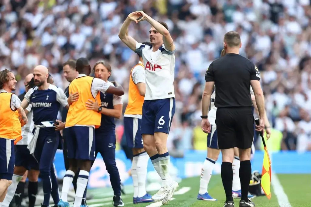 Jogador do Tottenham, com a camisola 6, celebra com as mãos no alto diante dos adeptos, junto à linha lateral e a equipa técnica