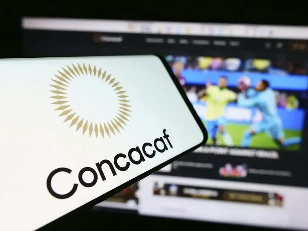 Smartphone com o logótipo da Concacaf em primeiro plano, com um site de futebol desfocado no ecrã ao fundo