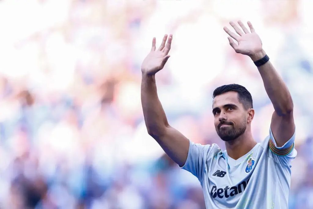 Jogador de equipamento cinzento do FC Porto, com braços no ar, a acenar aos adeptos em estádio