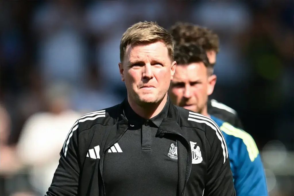 Treinador de casaco preto com logótipo do Newcastle, Adidas, a olhar em frente, com outro membro da equipa ao fundo