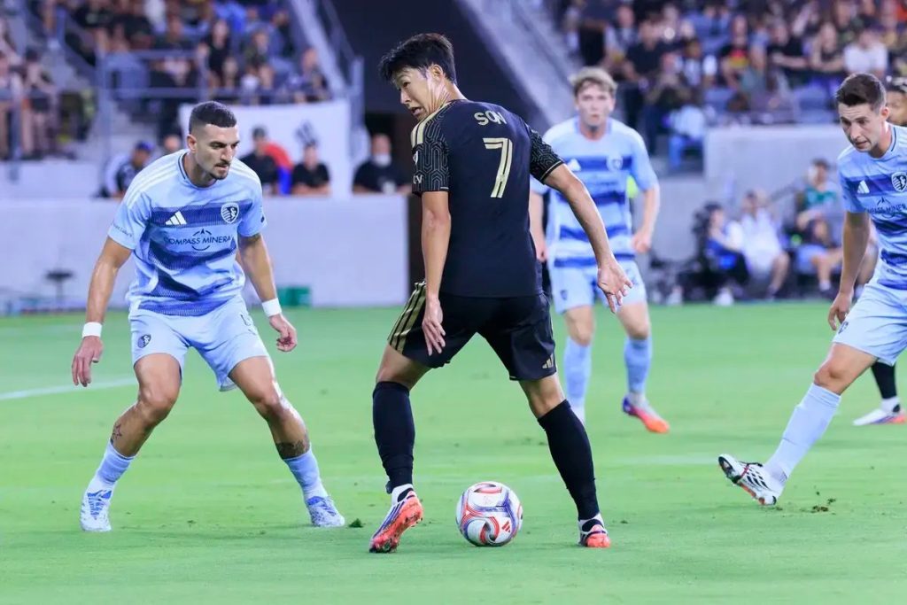 Jogador de preto com o número 7 e as iniciais "SW" controla a bola num jogo da MLS, rodeado por defesas de azul-claro.