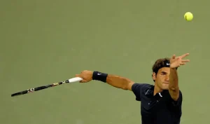 Tennis player in navy Nike shirt and headband tosses a ball and swings his racket during a match on a green court.