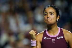 Alexandra Eala celebrating with a clenched fist during a tennis match, wearing a maroon top with BPI and Globe sponsor logos.