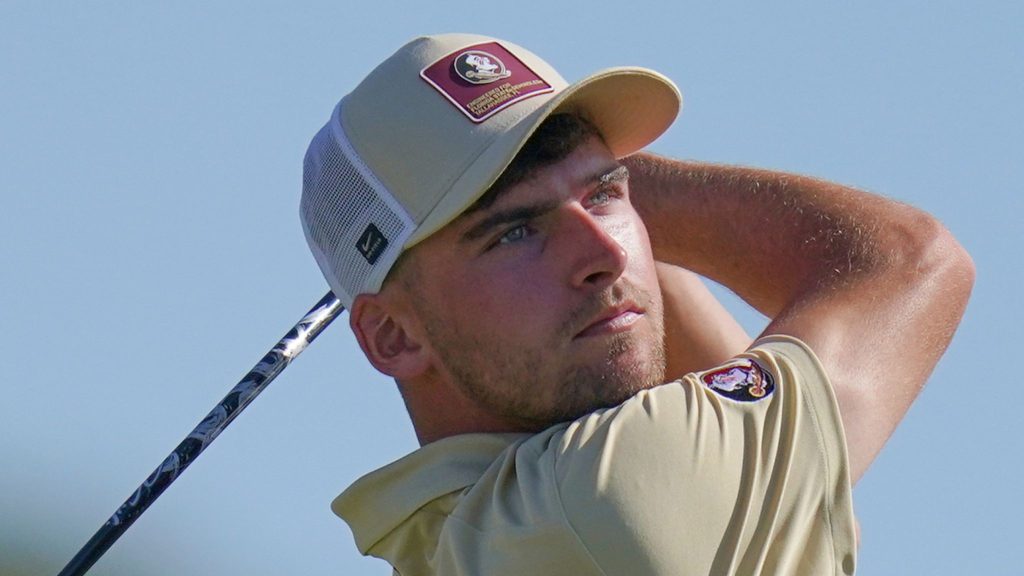 Golfer in a cream cap with a Florida State logo and cream shirt, swinging a club under a clear blue sky