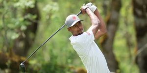 A golfer in a white shirt and cap swinging a driver on a tree-lined course, as Tennessee's men's golf team competes in Knoxville