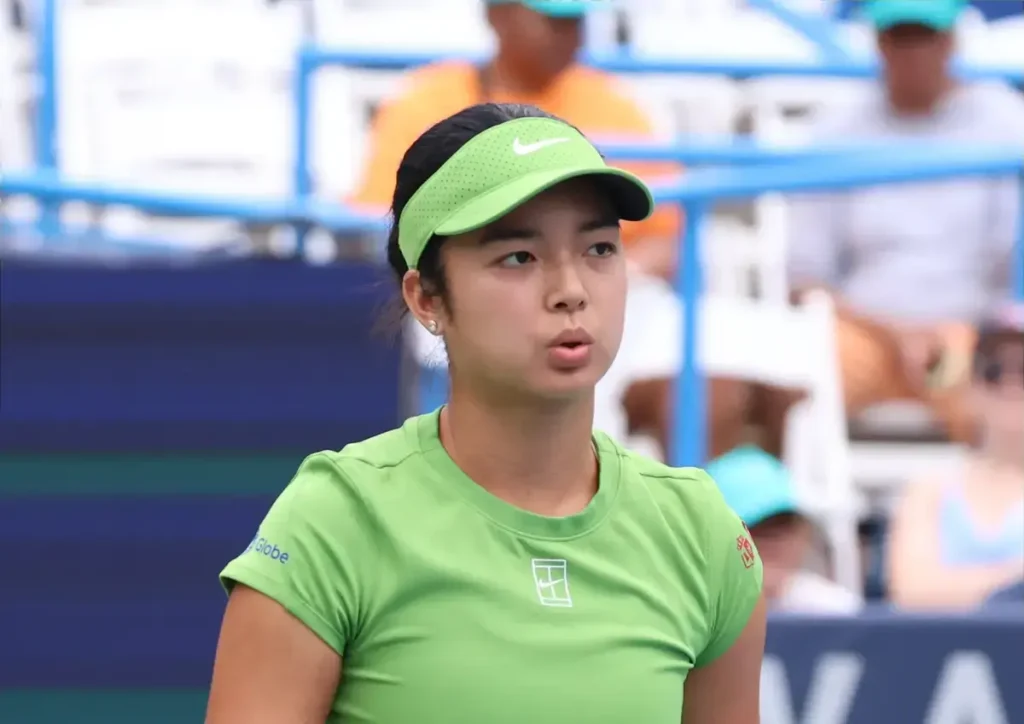 Alexandra Eala in a green Nike visor and matching shirt during a tennis match, looking focused on court.