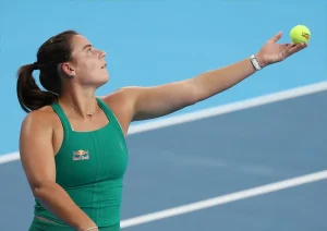Tennis player in green Red Bull top tossing a yellow ball before serving on a blue court, Emma Navarro shown mid-toss.