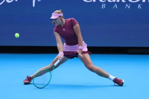 Mirra Andreeva in maroon and pink kit stretches low to return a forehand on a blue hard court, Credit One Bank backdrop