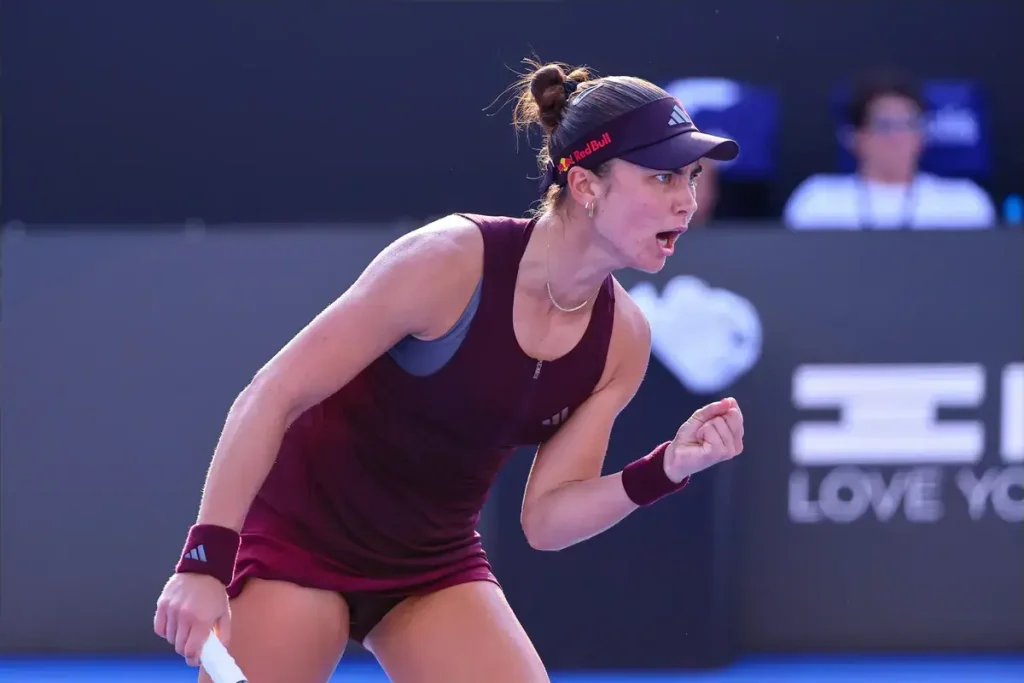 Tennis player in maroon Adidas kit and Red Bull visor fist-pumping on court at the Guadalajara Open, with a Love Yo banner behind