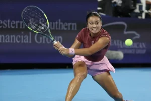 Tennis player in a maroon top and pink skirt hitting a backhand on a blue court, with a Western & Southern Financial Group banner behind her