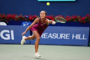 Leylah Fernandez in a maroon outfit lunges for a low forehand return on a hard court at the Singapore Open, with flowers and sponsor signage behind her.
