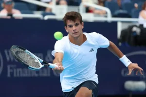 Tennis player in white Adidas shirt and wristband hitting a forehand with a blue-and-black racket at a Western & Southern Financial event.