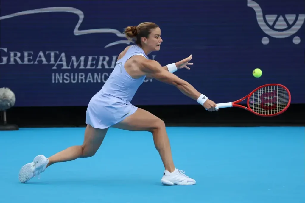 Tennis player in a light blue dress and white shoes lunging to hit a forehand, red Wilson racket, with a Great American Insurance sign behind her