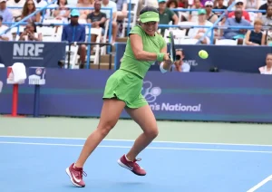 Alexandra Eala in a green Nike outfit and visor, swinging a forehand on a blue hard court at the Citi Open, crowd watching behind.