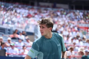Matteo Arnaldi in a teal EA7 shirt, looking intently during a match at the ATP Tokyo tournament with packed stands behind him.