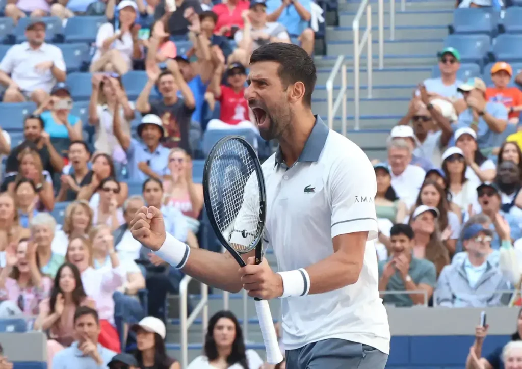Tennis player in a white Lacoste shirt and headband, roaring and clenching his fist while holding a racket, crowd cheering behind him