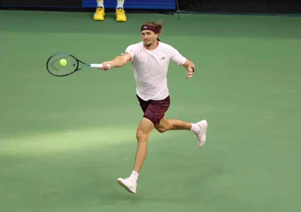 Alexander Zverev in white and maroon hits a forehand on a green hard court at the China Open tennis tournament.