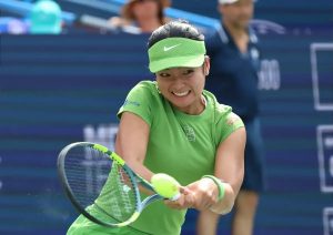 Tennis player in lime green Nike visor and shirt hitting a forehand at a tournament, with a blue court backdrop