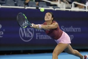Tennis player in maroon top and pink skirt stretching for a backhand return at a WTA match, with "Southern Financial" signage behind her.