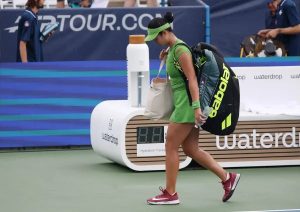 Tennis player in green visor, green dress and Babolat bag walking past a Waterdrop hydration tracker on court