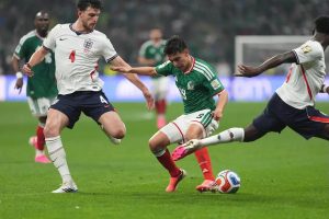 England's No. 4 Declan Rice (white kit) challenges Mexico's No. 13 in green during a match, with a white-shirted England player nearby.