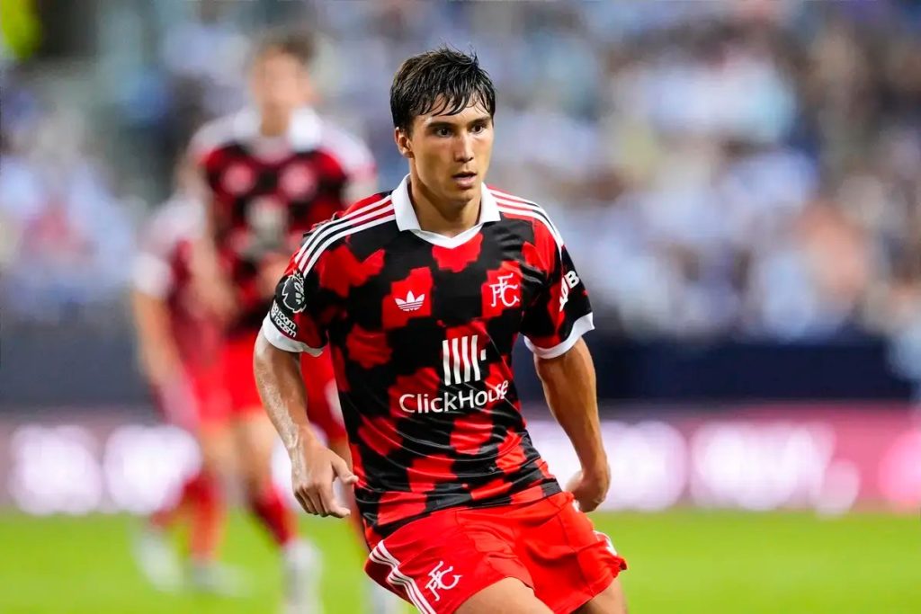 Young male footballer in red and black checkered kit with ClickHouse sponsor, playing on the pitch during a match.