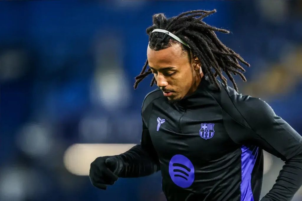 Dreadlocked player in black Barcelona training top warming up on a blurred stadium background, matching the article about Jules Koundé's possible January sale.