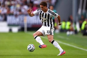 Juventus player in black and white striped kit, number 10, dribbling the ball on a green pitch during a match.