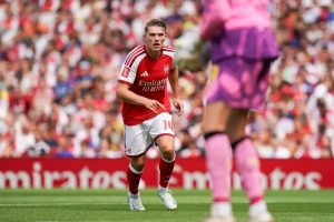 Arsenal player in red and white home kit with number 10 on the pitch during a match, goalkeeper in pink blurred in foreground