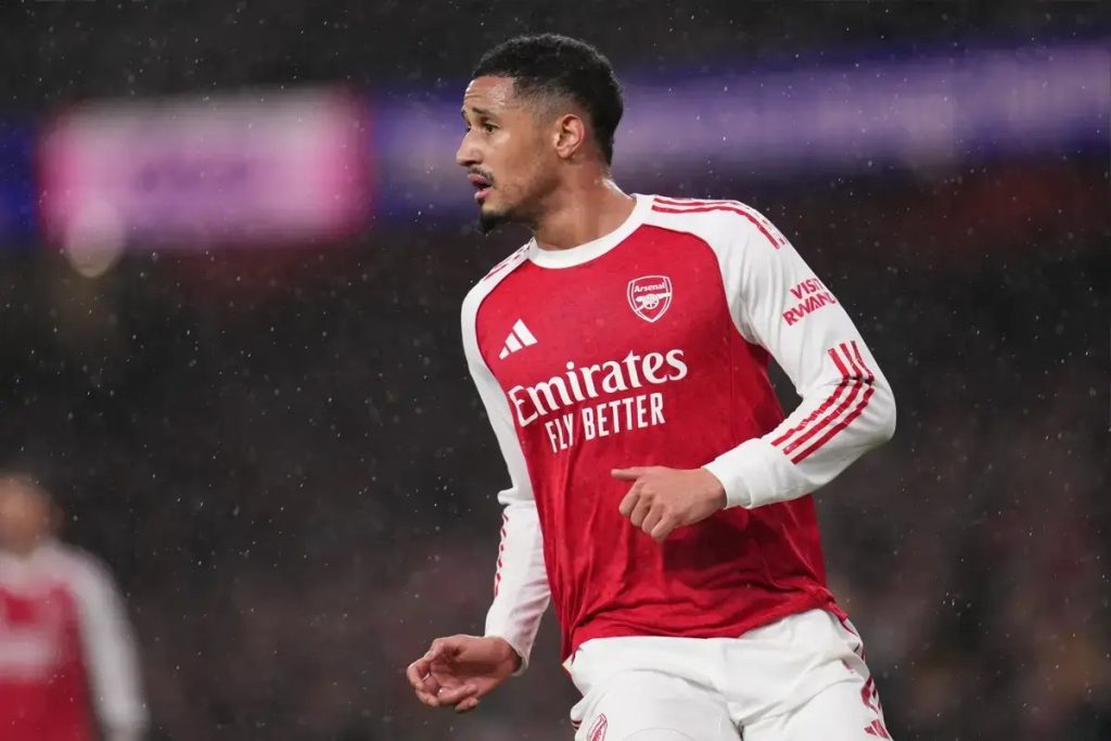 Arsenal defender in red and white home kit with Emirates sponsor, mid-action on a rainy night at the stadium