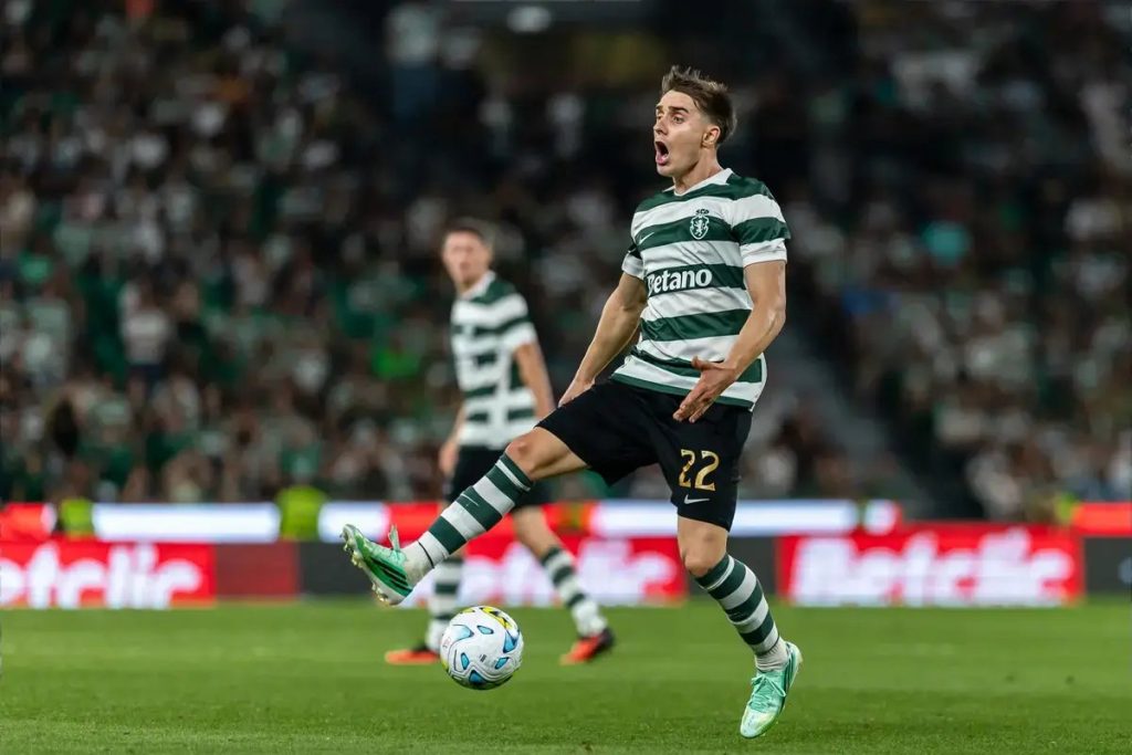 Sporting CP player number 22 in green-and-white stripes shouting and kicking the ball during a match at a packed stadium