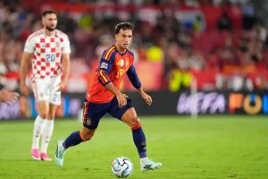 Spain midfielder in red and navy kit dribbling the ball past a Croatia player in a white checkerboard shirt during a match