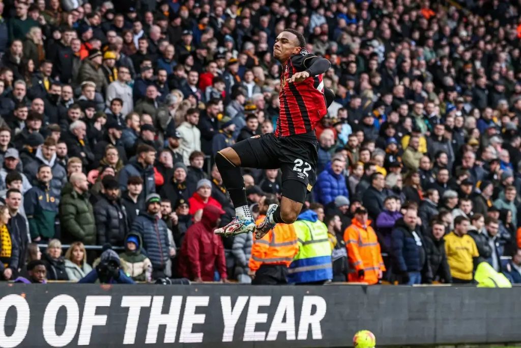 Player in red and black striped shirt and number 22 leaping mid-celebration in a packed stadium stand, with a crowd behind him