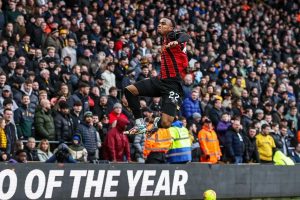Player in red and black striped shirt and number 22 leaping mid-celebration in a packed stadium stand, with a crowd behind him