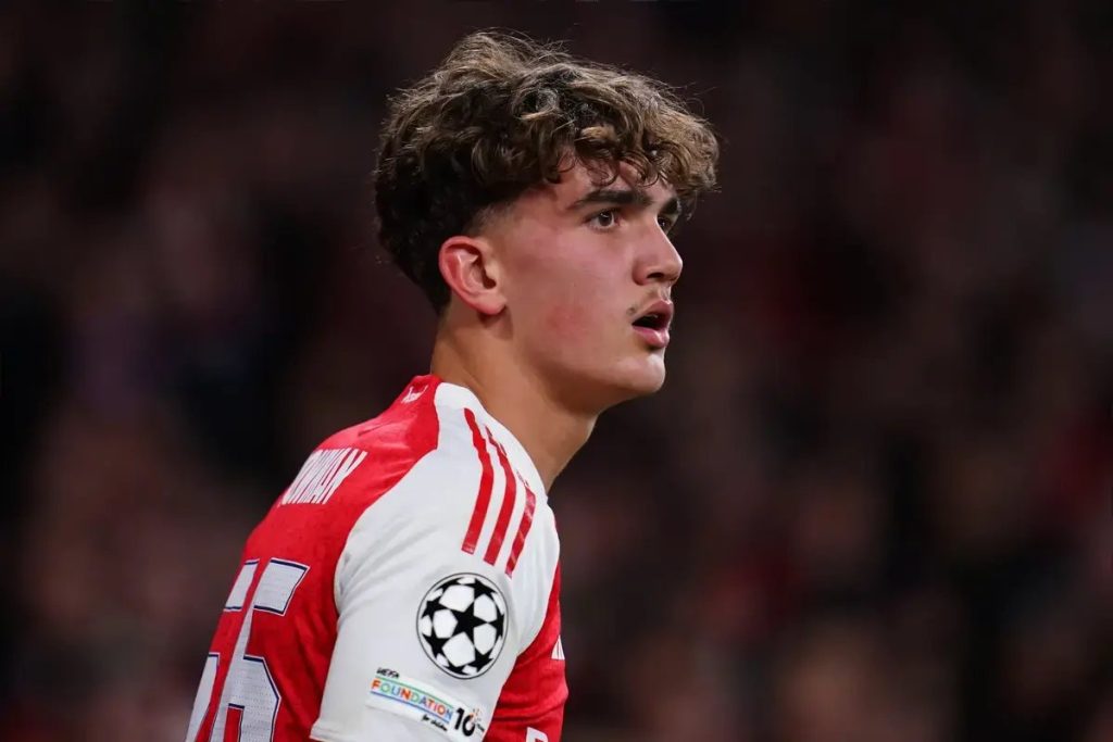 Young footballer in red and white Arsenal kit with Champions League badge, curly hair, looking intently off to the side in a stadium
