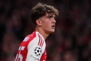 Young footballer in red and white Arsenal kit with Champions League badge, curly hair, looking intently off to the side in a stadium