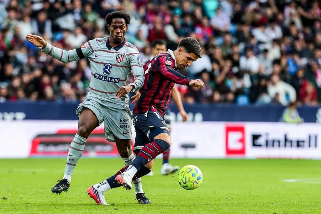 Jogador do Atlético de Madrid, de equipamento cinzento, disputa a bola com adversário do Levante de camisola listrada em vermelho e azul, num jogo da LaLiga.