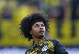 Man with voluminous curly hair and black headband in a black and yellow BVB 09 training top, looking upward at a stadium