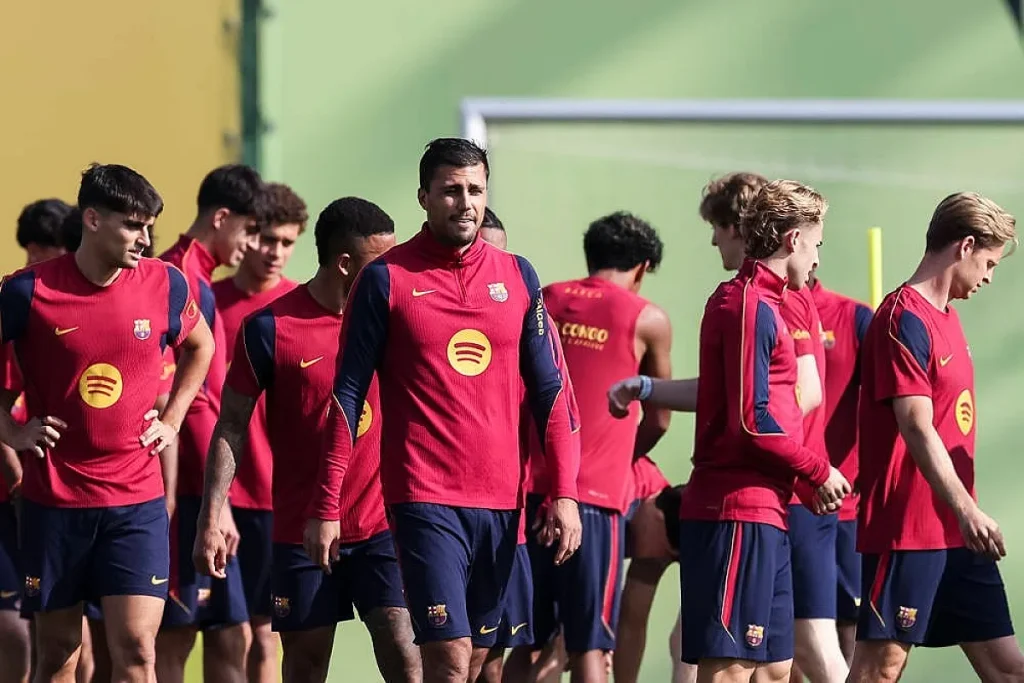 Jogadores do FC Barcelona com equipamento de treino vermelho e azul-marinho, num treino ao ar livre.