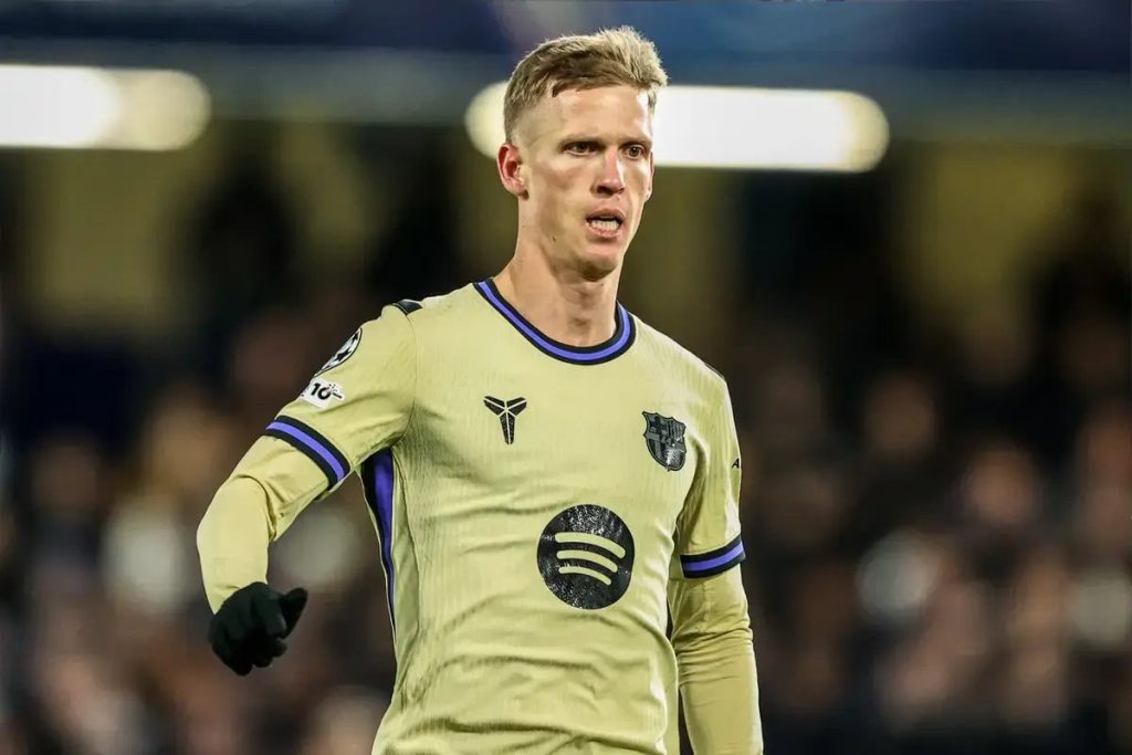 Footballer in gold-and-purple Barcelona away kit with black gloves, looking ahead during a night match. Article is about Dani Olmo's transfer talks.