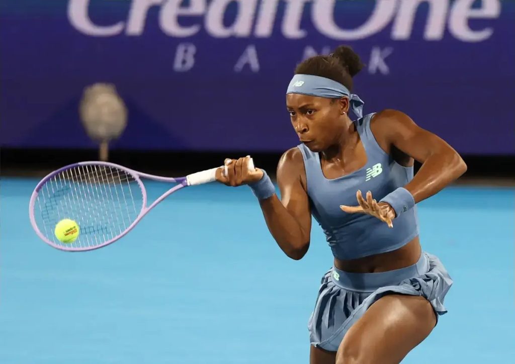 Tennis player in blue New Balance outfit and headband hits a forehand on a blue court under a CreditOne Bank sign