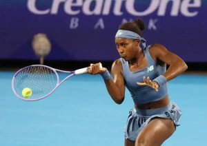 Tennis player in blue New Balance outfit and headband hits a forehand on a blue court under a CreditOne Bank sign