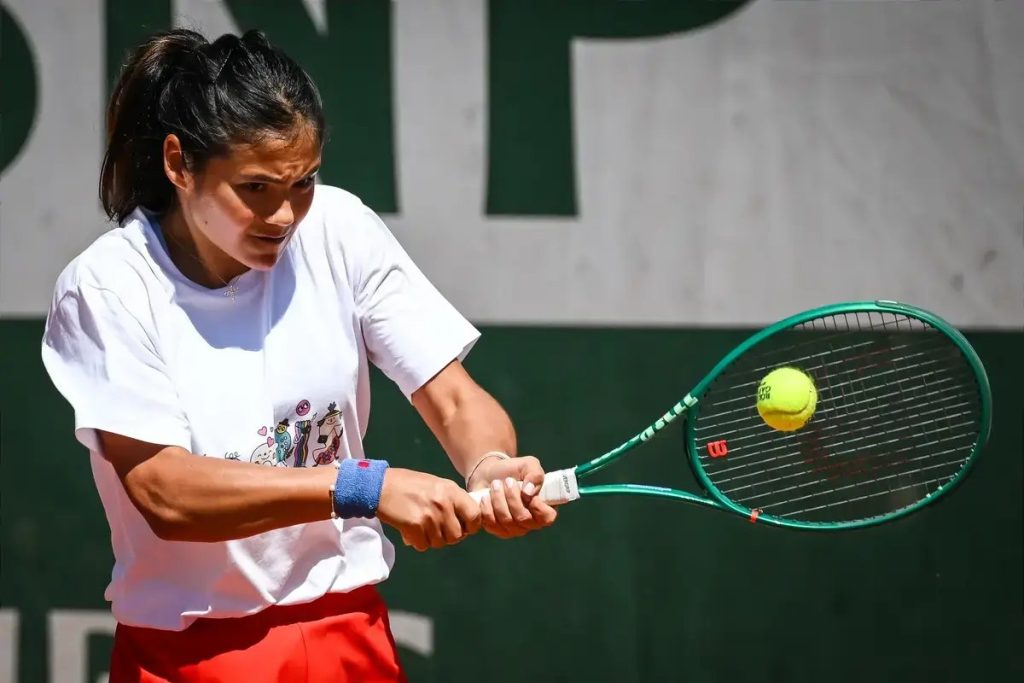 A woman with a ponytail in a white tee and red skirt hits a forehand with a green Wilson racquet on a clay court.