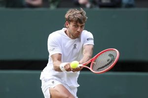 Tennis player in white On apparel hitting a backhand with a red racket on a grass court, ball in view. Article subject: Flavio Cobolli.