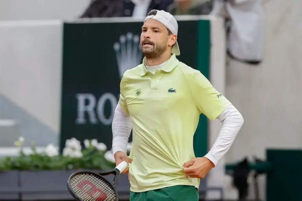 Tennis player in a light green Lacoste polo and white cap holding a Wilson racket on a clay court, with a Rolex sign behind him.