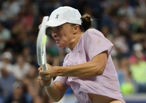 Iga Swiatek in a pink top and white On cap hitting a backhand during a match at Wuhan 2025