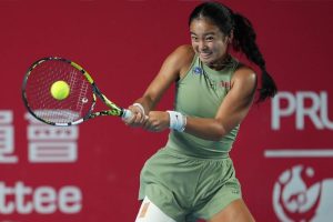 Alex Eala in a green outfit hitting a backhand with a Babolat racket at a tournament with red court backdrop