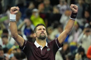 Tennis player in maroon Lacoste polo and wristbands raises both fists in celebration in a crowded stadium at the China Open